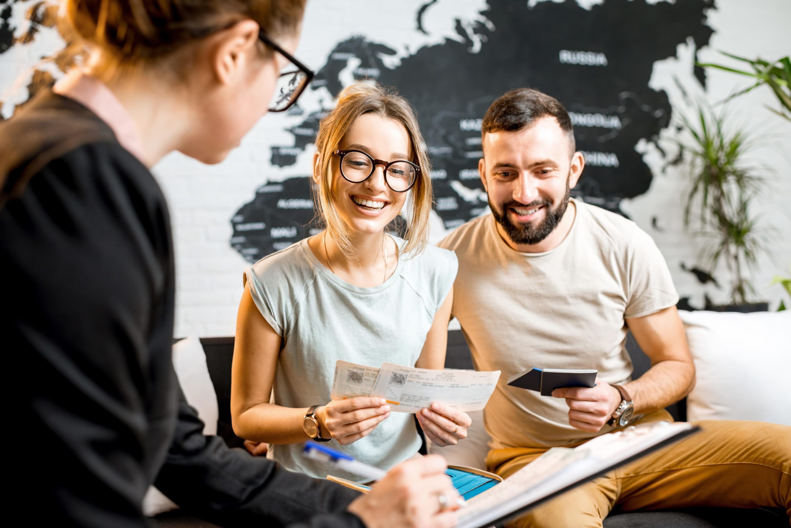 Pareja joven planificando su viaje de Latinoamérica a España en una agencia de viajes, revisando boletos y pasaportes con un agente de viajes.